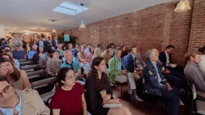 Wide view of a corporate audience using grey industrial-style rental chairs in a Midtown Manhattan loft with a skylight.