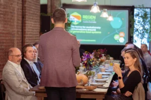 A keynote speaker presenting to a seated audience at LOFT39, utilizing in-house rustic dining tables and professional A/V projector rentals.
