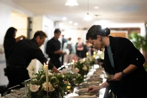 Event staff setting up premium flatware, glassware, and floral centerpieces on a long rental communal table in a Manhattan loft.