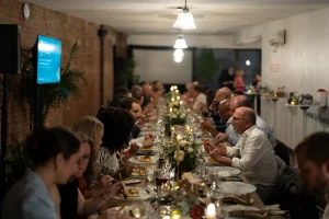 A seated gala dinner at LOFT39 featuring in-house communal tables, plateware rentals, and wall-mounted TV monitors for presentations.