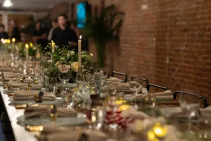 A long-table feasting setup at LOFT39 featuring elegant floral arrangements, tapered candles, and exposed brick walls for a milestone dinner.