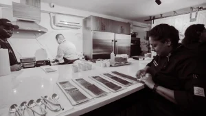 A professional private chef team preparing a multi-course tasting menu on the large marble island in the LOFT39 2nd-floor kitchen.