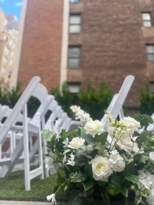 A crisp daytime view of a rooftop wedding ceremony space with a synthetic grass lawn and a floral altar.