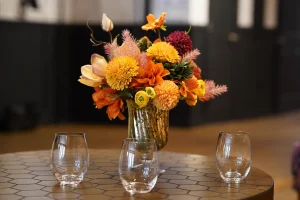 A long farmhouse-style wedding table decorated with vibrant orange linens and tropical florals in a New York City loft.