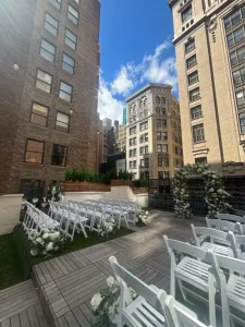 Wide-angle shot of a rooftop wedding ceremony location featuring a wooden deck and a lush floral arch.