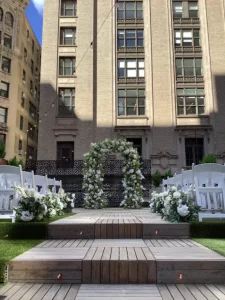 Nighttime rooftop wedding reception featuring white garden chairs and warm string lighting over a wooden deck.