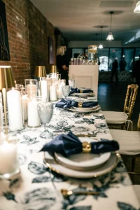 A rustic-modern wedding table setup featuring green napkins, farmhouse tables, and warm brick walls.