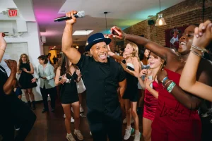 Smiling teenagers dancing with glow sticks during a vibrant evening Bat Mitzvah reception in an NYC landmark building.