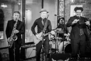 Editorial-style black and white photo of a full cover band rocking out under stage lights at a private 30th birthday celebration.